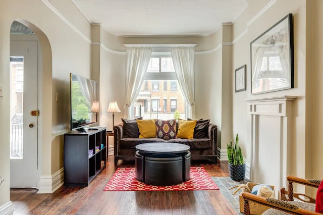 living area with arched walkways, crown molding, baseboards, and wood finished floors