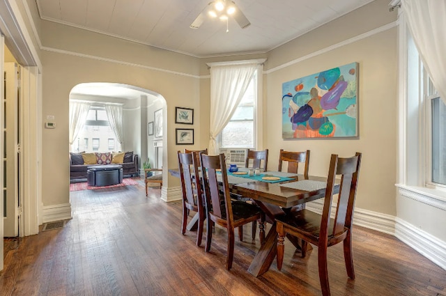 dining space featuring ornamental molding, arched walkways, dark wood-style flooring, and plenty of natural light