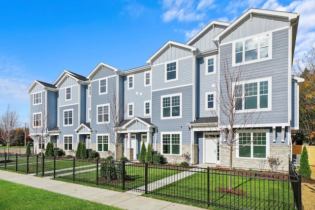 townhome / multi-family property with board and batten siding, a front yard, and stone siding