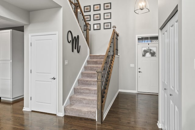 entrance foyer featuring stairs, dark wood-style flooring, a towering ceiling, and baseboards