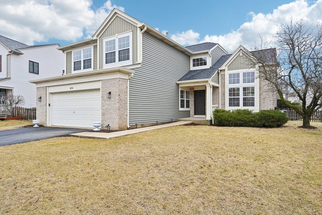 traditional-style house with board and batten siding, a front lawn, aphalt driveway, brick siding, and a garage