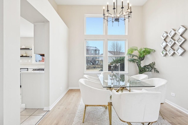 dining space featuring baseboards, a towering ceiling, light wood finished floors, and an inviting chandelier