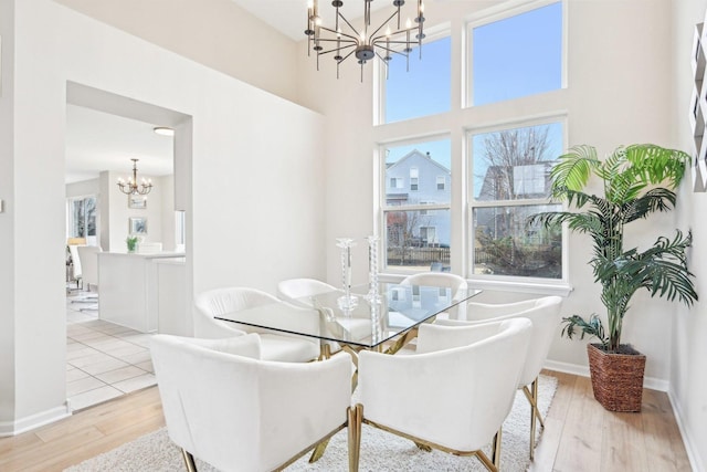 dining area with baseboards, a high ceiling, wood finished floors, and an inviting chandelier