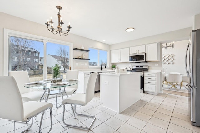 kitchen featuring a center island, an inviting chandelier, stainless steel appliances, white cabinetry, and light tile patterned flooring