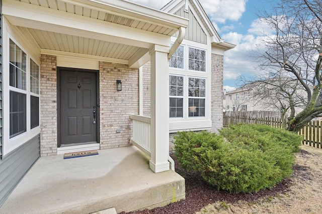 property entrance featuring board and batten siding, covered porch, brick siding, and fence