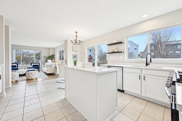 kitchen with light tile patterned floors, a kitchen island, appliances with stainless steel finishes, white cabinetry, and a sink