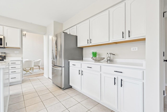 kitchen with light countertops, white microwave, freestanding refrigerator, white cabinetry, and light tile patterned flooring