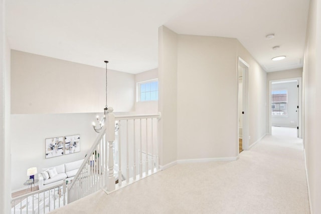 corridor featuring an inviting chandelier, baseboards, carpet flooring, and an upstairs landing