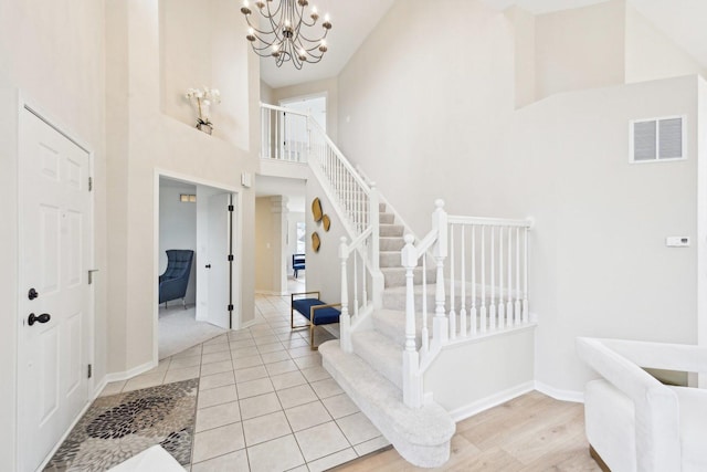 entryway with a towering ceiling, baseboards, visible vents, stairway, and an inviting chandelier