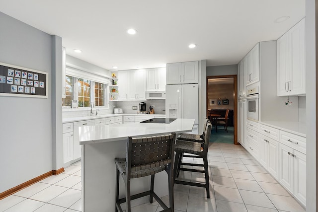 kitchen featuring light tile patterned floors, white appliances, a breakfast bar, a sink, and decorative backsplash