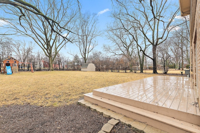 view of yard featuring fence, playground community, a wooden deck, a shed, and an outdoor structure