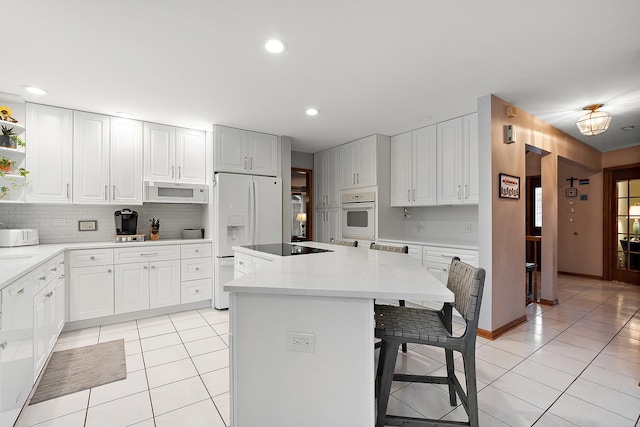 kitchen featuring white appliances, light tile patterned floors, a breakfast bar area, a center island, and light stone countertops