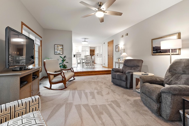 living area with visible vents, a ceiling fan, and light colored carpet