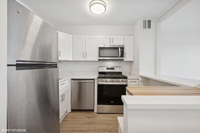 kitchen with visible vents, light stone counters, stainless steel appliances, light wood-style floors, and white cabinetry