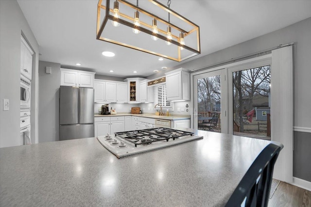 kitchen with white appliances, glass insert cabinets, hanging light fixtures, white cabinetry, and recessed lighting