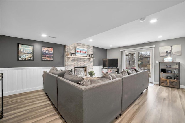 living area featuring a brick fireplace, wainscoting, visible vents, and wood finished floors