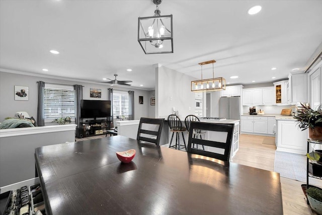 dining space with light wood finished floors, baseboards, ceiling fan with notable chandelier, crown molding, and recessed lighting