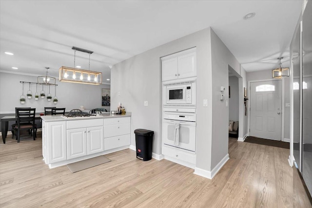 kitchen with a peninsula, white appliances, white cabinetry, baseboards, and light wood-style floors