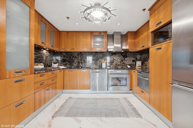 kitchen featuring marble finish floor, wall chimney range hood, dark stone countertops, and appliances with stainless steel finishes