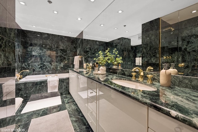 full bathroom featuring double vanity, a bath, a sink, marble finish floor, and tile walls