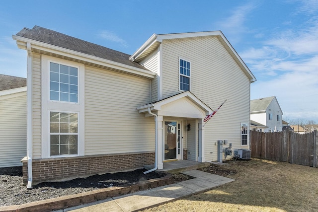 traditional-style home with central AC, brick siding, a shingled roof, and fence