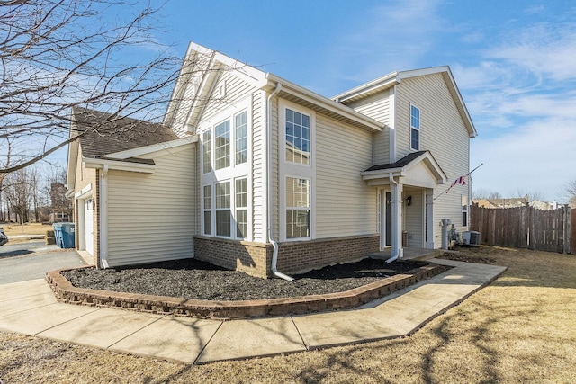 view of side of home featuring driveway, a garage, fence, central air condition unit, and brick siding