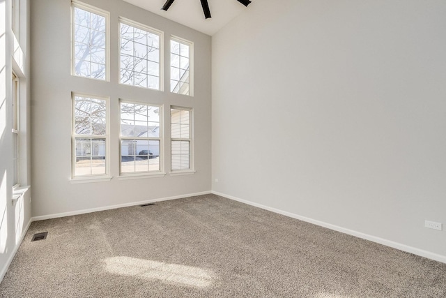 unfurnished room with carpet floors, visible vents, a high ceiling, a ceiling fan, and baseboards