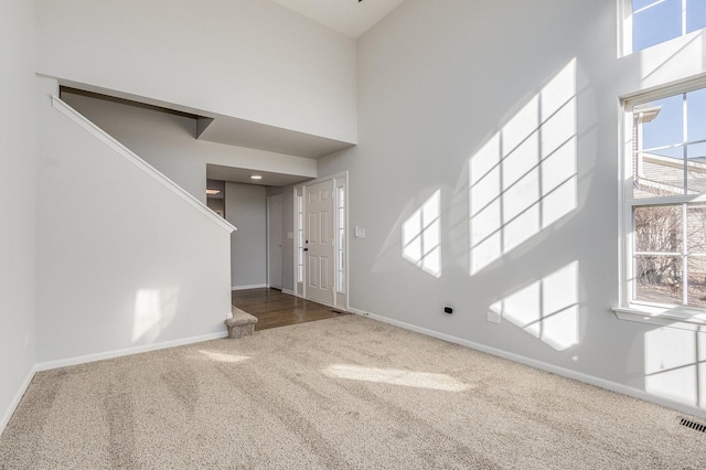 entryway with carpet, visible vents, a towering ceiling, and baseboards