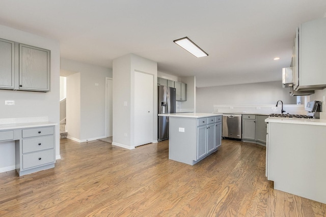 kitchen with a center island, stainless steel appliances, gray cabinets, light countertops, and wood finished floors