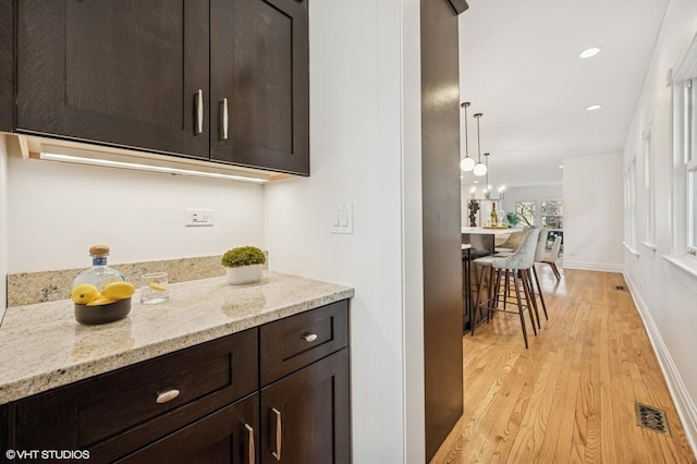 kitchen with light stone countertops, visible vents, baseboards, light wood-style flooring, and dark brown cabinetry