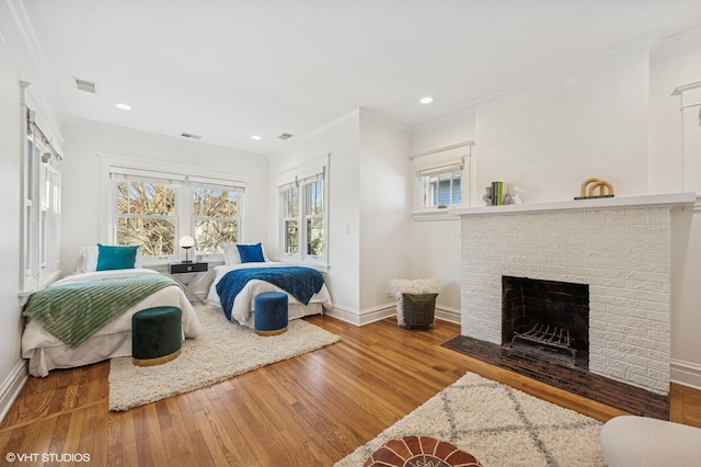 bedroom with visible vents, baseboards, wood-type flooring, crown molding, and a brick fireplace