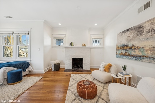 living room featuring wood finished floors, a brick fireplace, baseboards, and visible vents