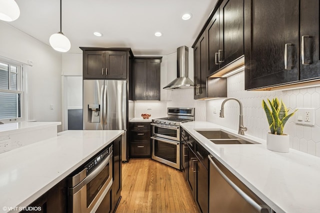 kitchen featuring a sink, stainless steel appliances, decorative light fixtures, wall chimney exhaust hood, and light wood-type flooring