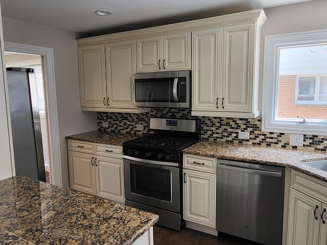 kitchen with dark wood-type flooring, dark stone countertops, stainless steel appliances, and decorative backsplash