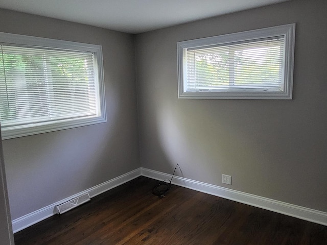 unfurnished room with dark wood-style floors, a healthy amount of sunlight, visible vents, and baseboards