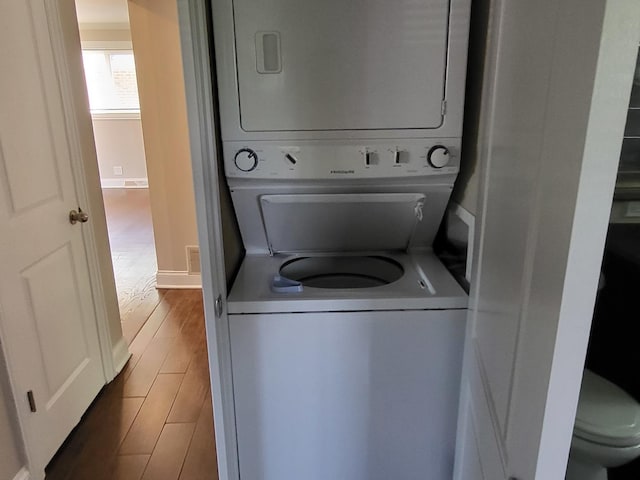 clothes washing area featuring stacked washing maching and dryer, baseboards, laundry area, and wood finished floors