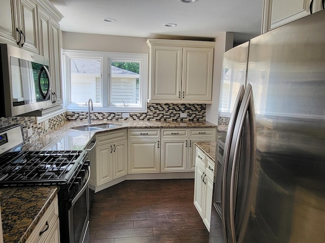 kitchen with a sink, appliances with stainless steel finishes, dark wood-style floors, tasteful backsplash, and dark stone countertops