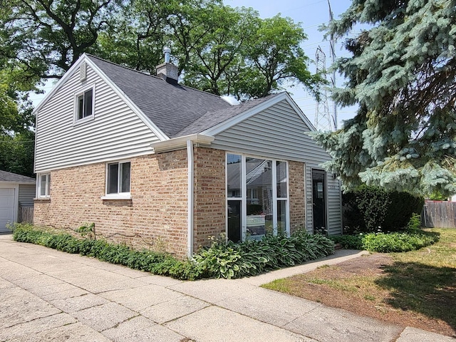 view of property exterior featuring an outbuilding, brick siding, a shingled roof, fence, and a chimney