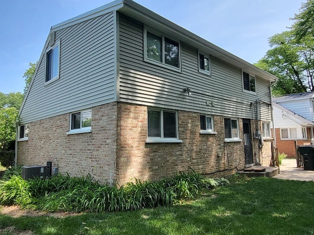 back of house featuring brick siding, a lawn, and central AC unit