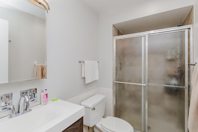 bathroom with tile walls, a stall shower, toilet, and vanity