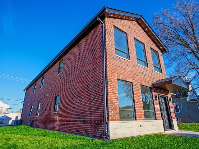 view of side of home featuring brick siding, a lawn, and central AC