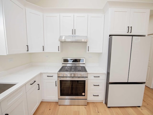 kitchen featuring under cabinet range hood, stainless steel range with gas cooktop, white cabinets, and freestanding refrigerator