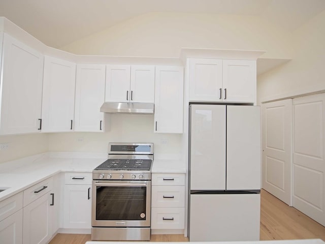 kitchen with white cabinets, freestanding refrigerator, vaulted ceiling, under cabinet range hood, and stainless steel range with gas stovetop