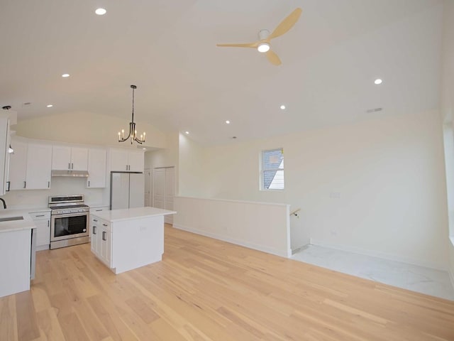 kitchen with a center island, freestanding refrigerator, white cabinets, under cabinet range hood, and stainless steel gas range oven