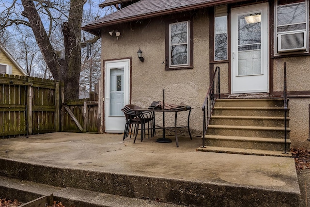 doorway to property featuring a shingled roof, a patio, fence, cooling unit, and stucco siding