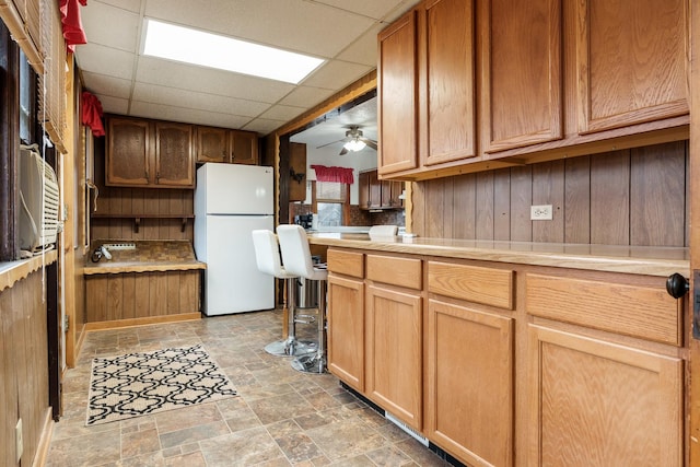 kitchen featuring a drop ceiling, ceiling fan, stone finish floor, freestanding refrigerator, and light countertops