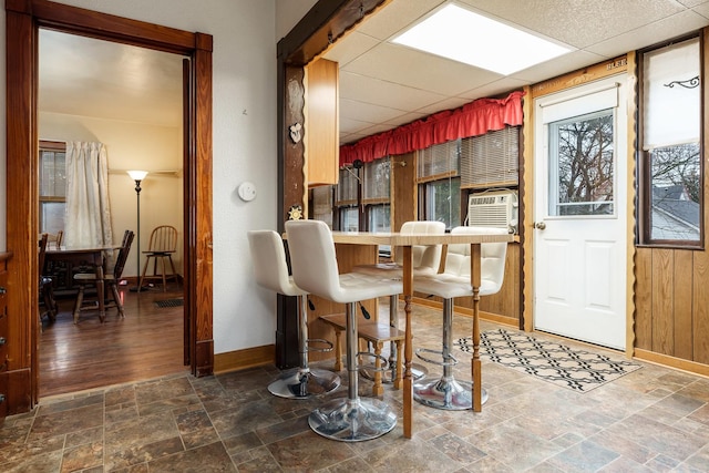 dining area featuring a paneled ceiling, baseboards, stone finish floor, and cooling unit