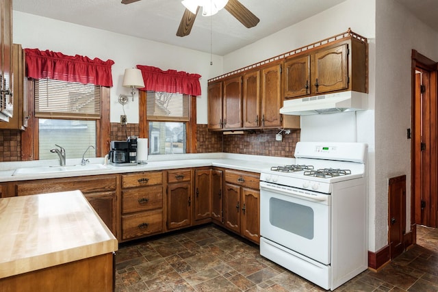 kitchen featuring white range with gas cooktop, brown cabinets, stone finish flooring, under cabinet range hood, and a sink