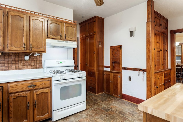 kitchen featuring white range with gas stovetop, brown cabinets, stone finish floor, and under cabinet range hood