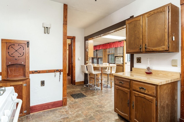 kitchen with cooling unit, light countertops, range, stone finish flooring, and brown cabinetry